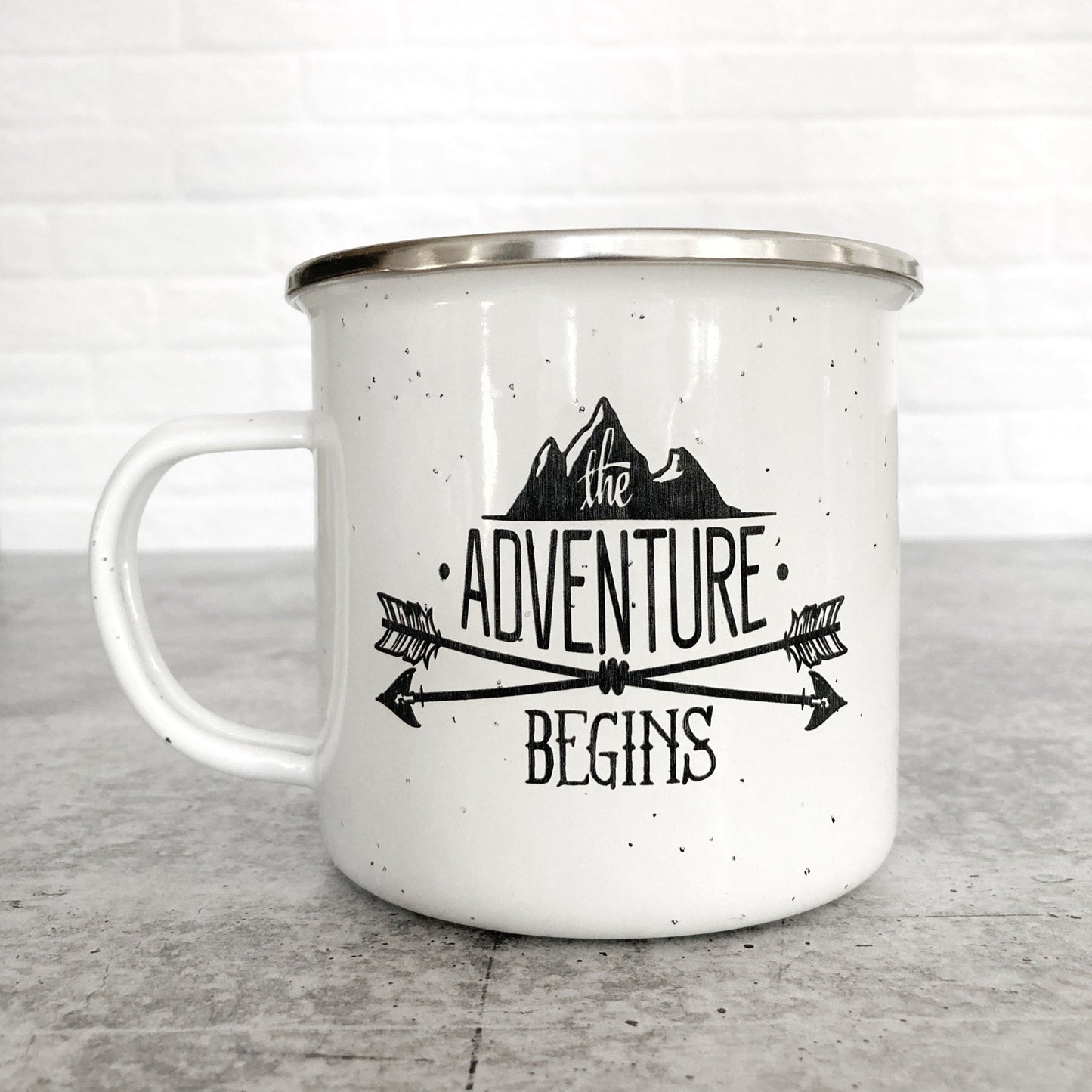 The Adventure Begins Mountain Design on a white enamel mug
